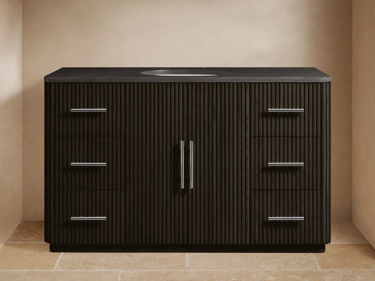 Dark brown fluted Finnley Wide Single Vanity with dark stone top, oval sink, chrome faucet, 2 left drawers, 3 right drawers, 2 center doors with chrome pulls.