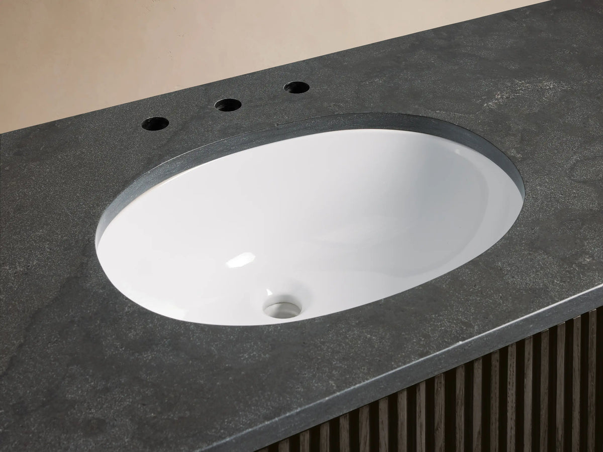 Finnley Wide Single Vanity close-up. Dark gray honed stone countertop, white oval undermount sink, chrome faucet.