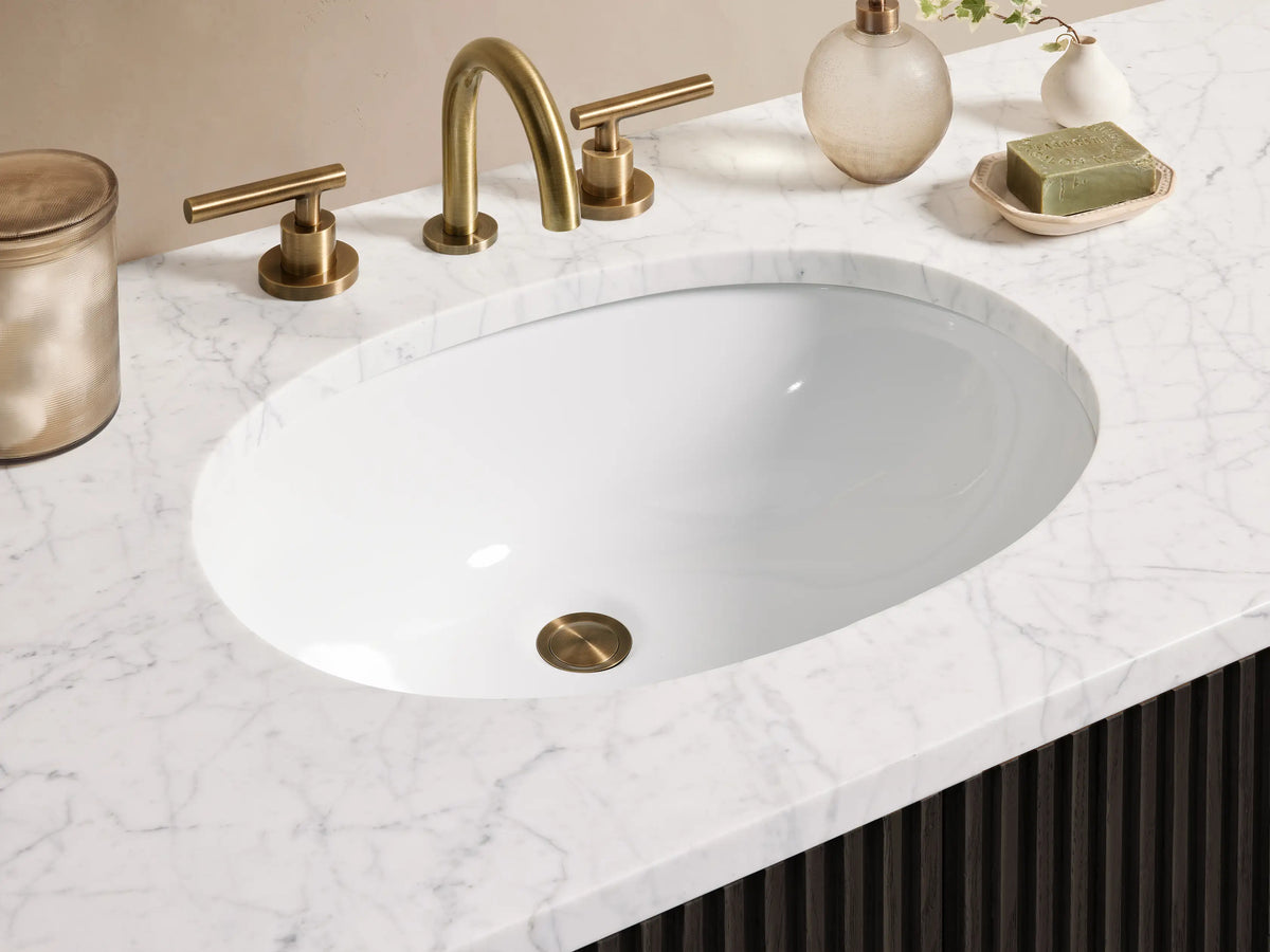 Finnley Single Wide Vanity with dark wood front, vertical grooves, brass hardware, marble top, and oval sink, set against a tan wall.