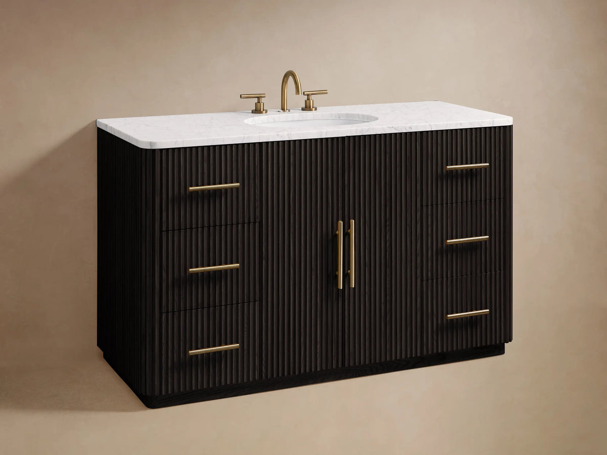 Finnley Single Wide Vanity with open ribbed oak drawer, gold handle. White Carrara marble top with visible towels and toiletries.