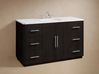 The Finnley Single Wide Vanity features a dark oak wood drawer with horizontal grooves, a silver handle, and a marble top. Inside are a folded towel and toiletries.