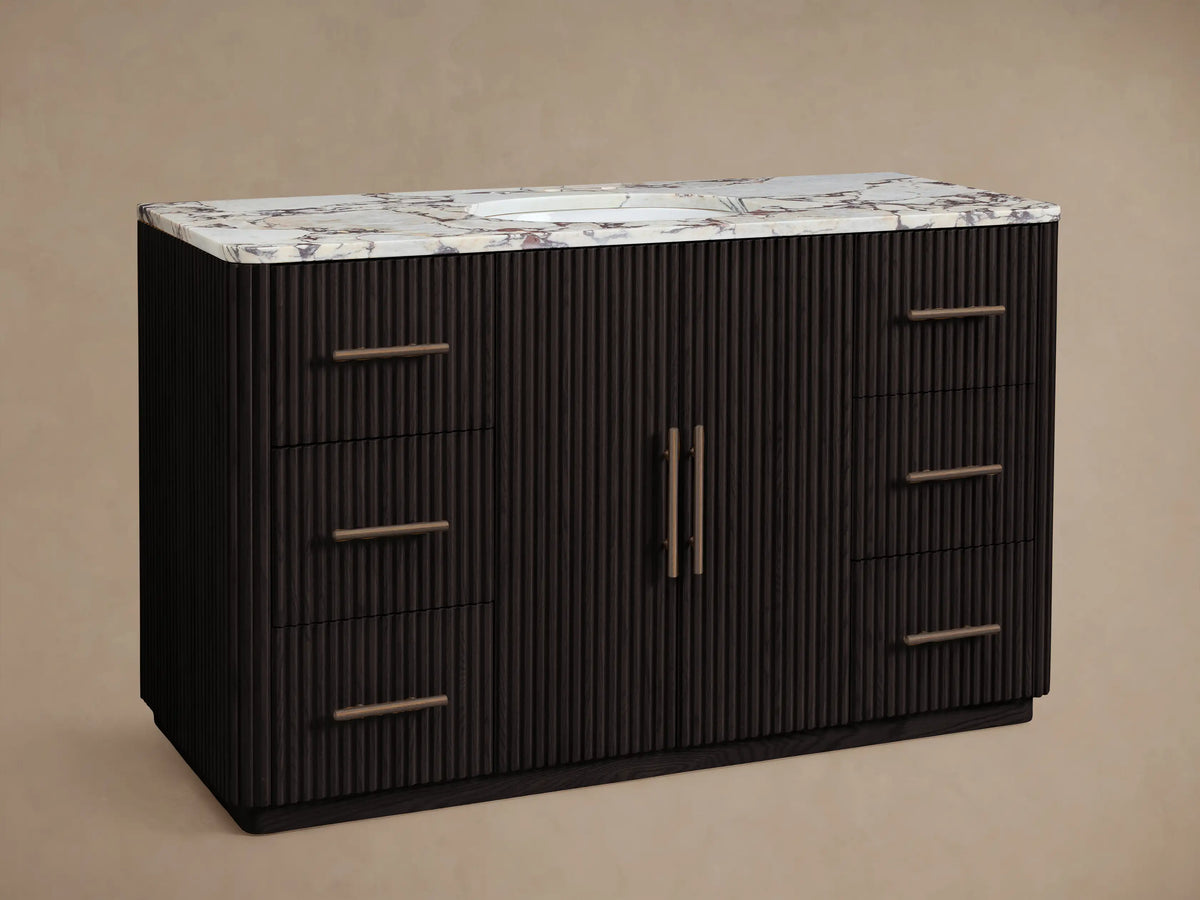 Finnley Wide Single Vanity: Dark fluted wood with white veined marble top, oval sink, bronze faucet, 6 drawers & 2 doors.