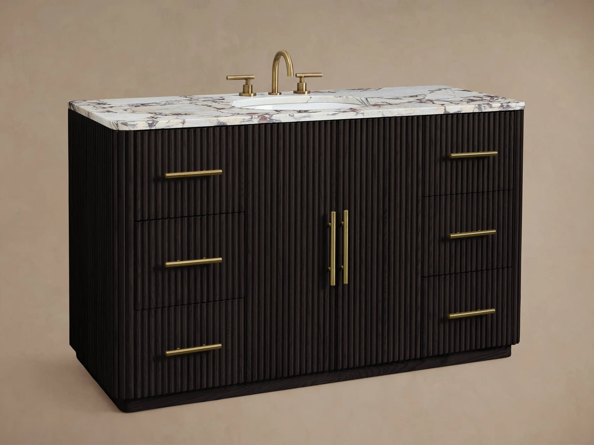 Finnley Wide Single Vanity: dark fluted cabinet, brass handles, white marble top with reddish veining, oval sink.