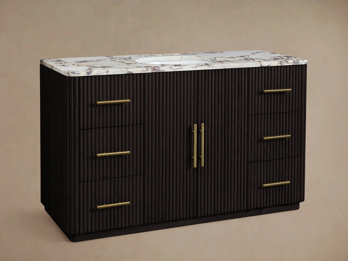Finnley Wide Single Vanity with dark fluted wood, white marble top, gold widespread faucet & hardware, oval sink, 6 drawers, 2 doors.