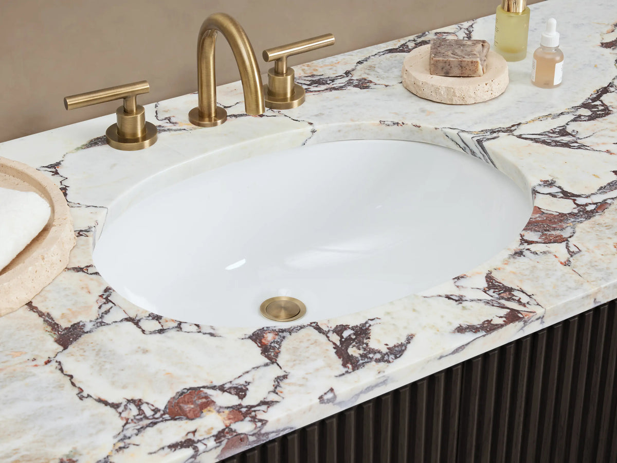 Finnley Wide Single Vanity: dark ribbed wood cabinet, light Carrara marble top with oval sink, brass hardware.