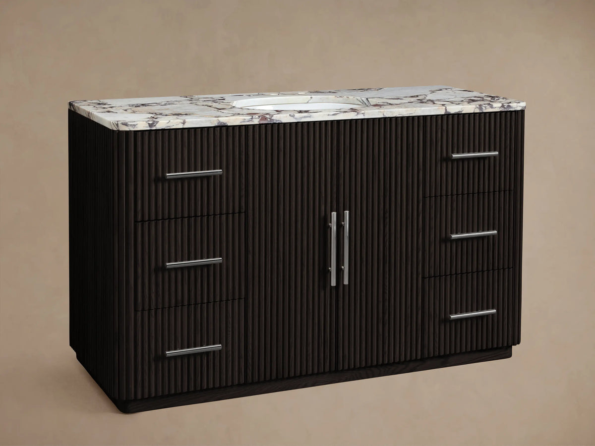 Finnley Wide Single Vanity: Dark fluted wood, white Carrara marble top, oval sink, chrome faucet, six chrome pulls.