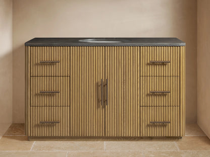 Finnley Wide Single Vanity: fluted light wood cabinet, dark stone top with oval sink, bronze faucet, and hardware in a bathroom.