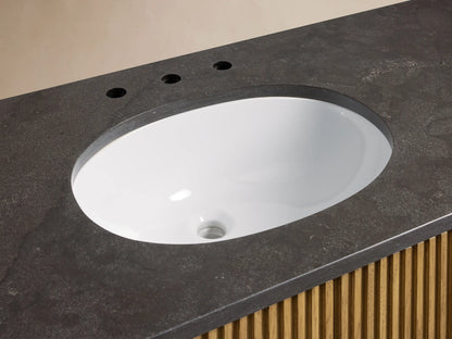 Finnley Single Wide Vanity with dark stone top, oval white ceramic sink, and dual brass faucets. Fluted wood base visible.