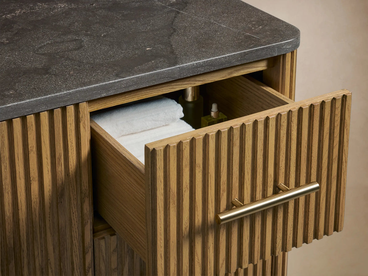 Finnley Single Wide Vanity detail showing oak wood texture, vertical grooves, and brass-finished handles with open door revealing shelves.