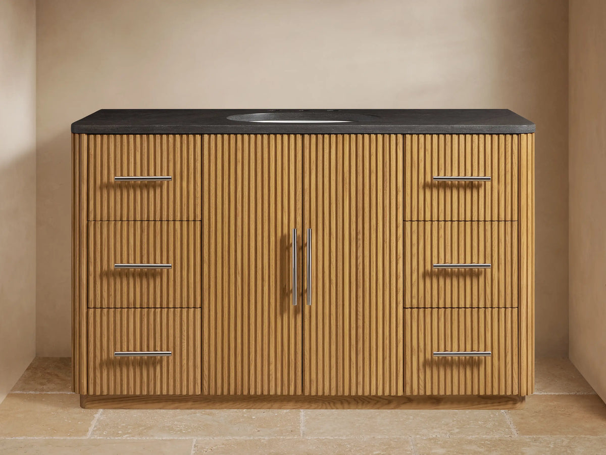 Finnley Single Wide Vanity in oak with vertical grooves, soft-close drawers, black stone top, silver hardware, ceramic sink.