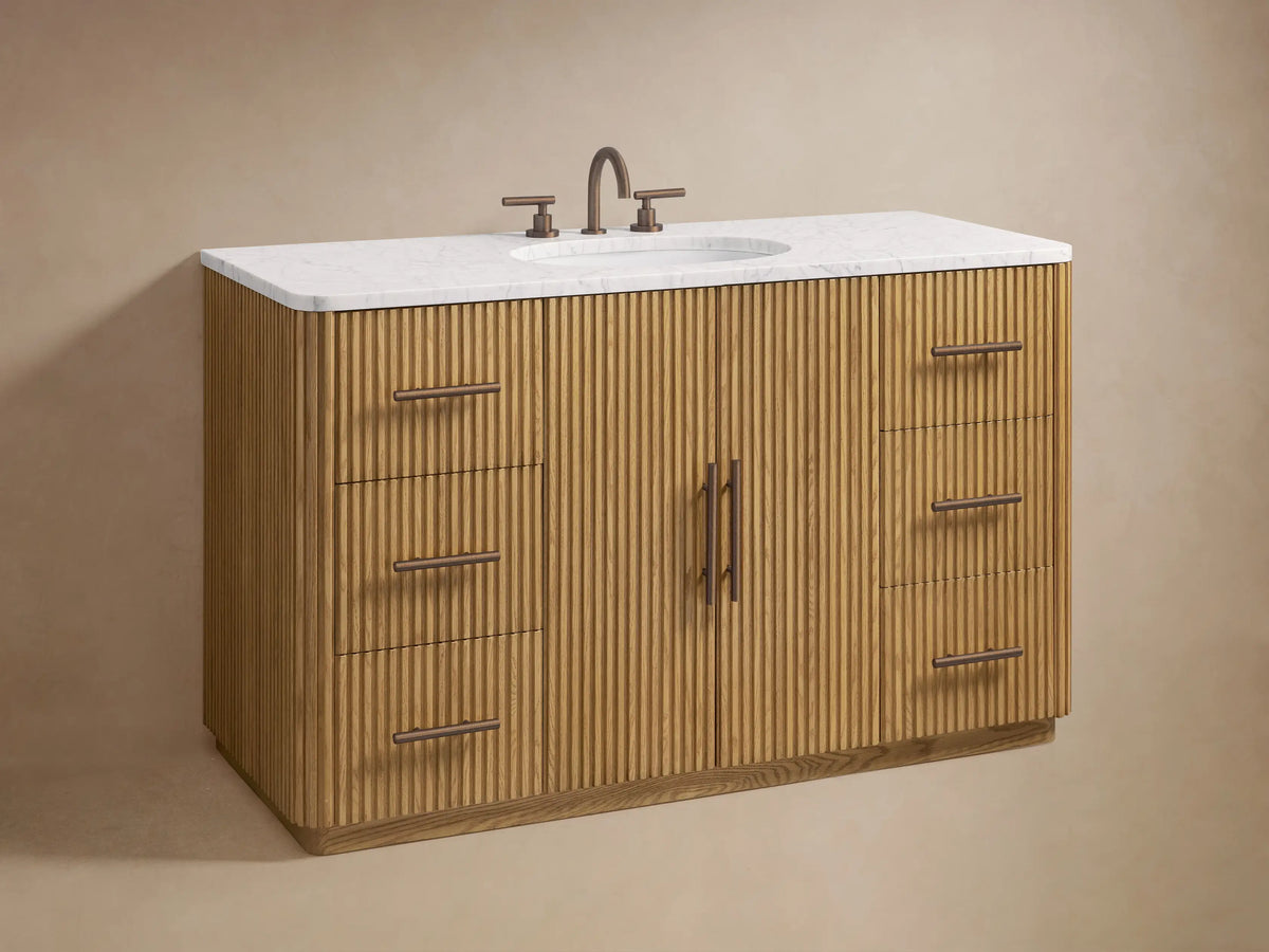 Close-up of Finnley Wide Single Vanity's fluted oak doors & drawers with Antique Bronze handles, showing shelves, box, & towels.