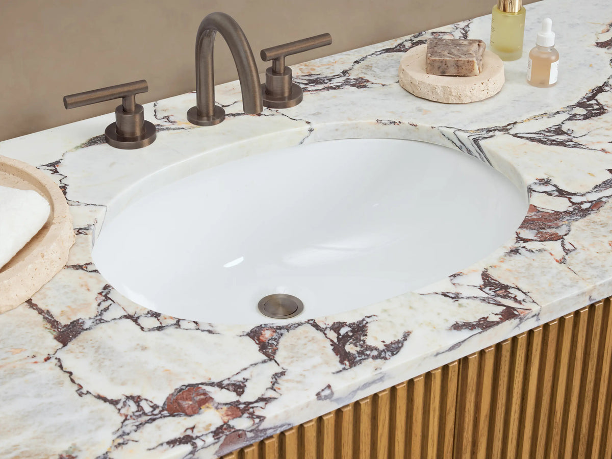 Finnley Wide Single Vanity: Front view. Fluted light oak base, white marble top with purple veins, oval sink, and dark bronze hardware.