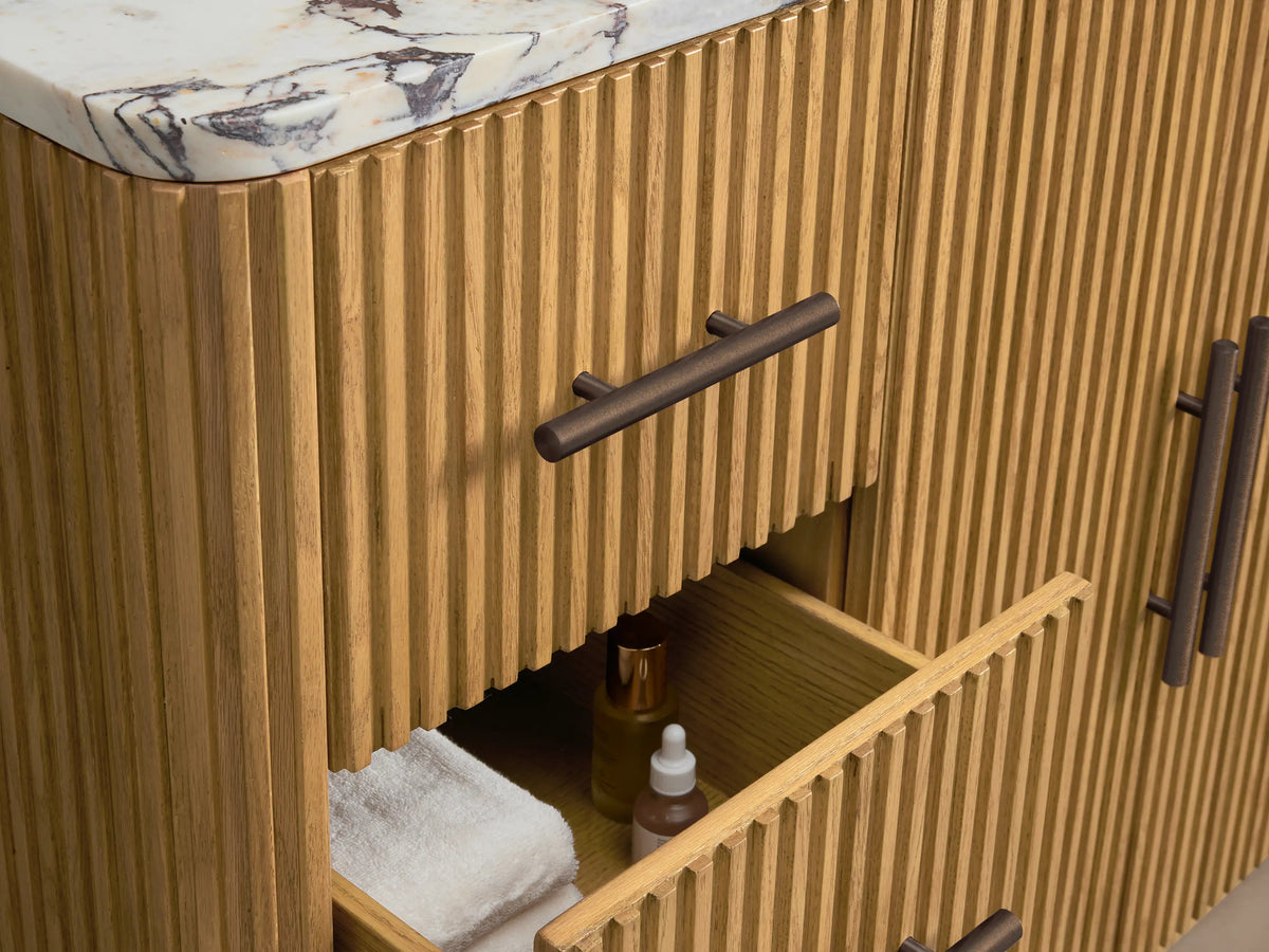 Close-up of Finnley Single Vanity. White oval sink set in a cream and reddish-brown veined marble top, with fluted oak cabinet below.