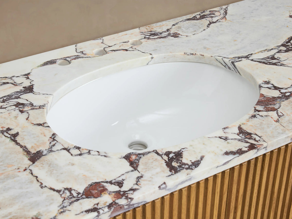 Close-up of Finnley Wide Single Vanity. White oval sink, brass faucet, white & reddish-brown veined marble top, slatted wood base.
