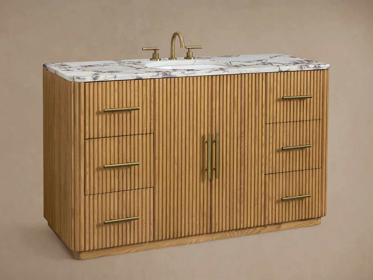 Finnley Wide Single Vanity, close-up of light oak fluted door with brass handle, slightly open, revealing white towels on a shelf.