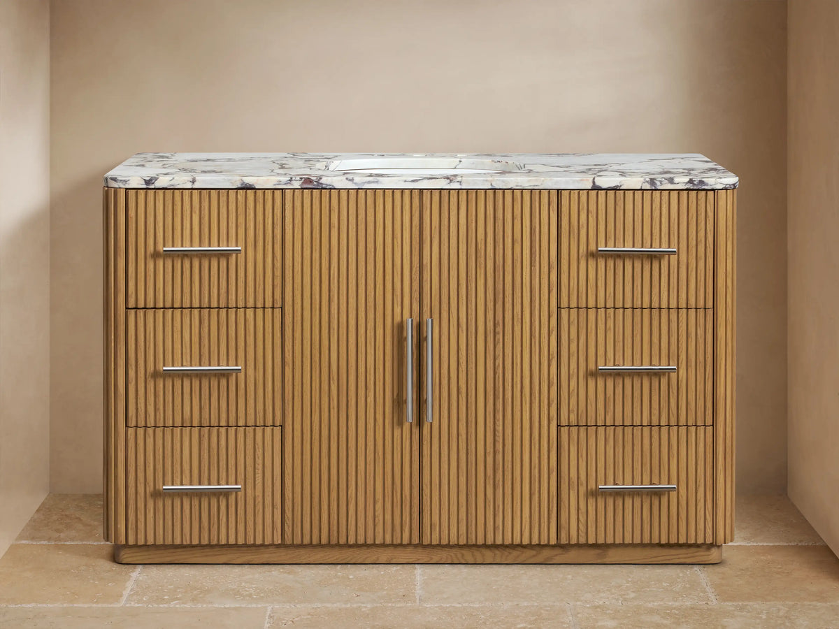 Finnley Wide Single Vanity. Close-up of fluted oak wood, white marble top. Drawer partially open with towel & bottles.
