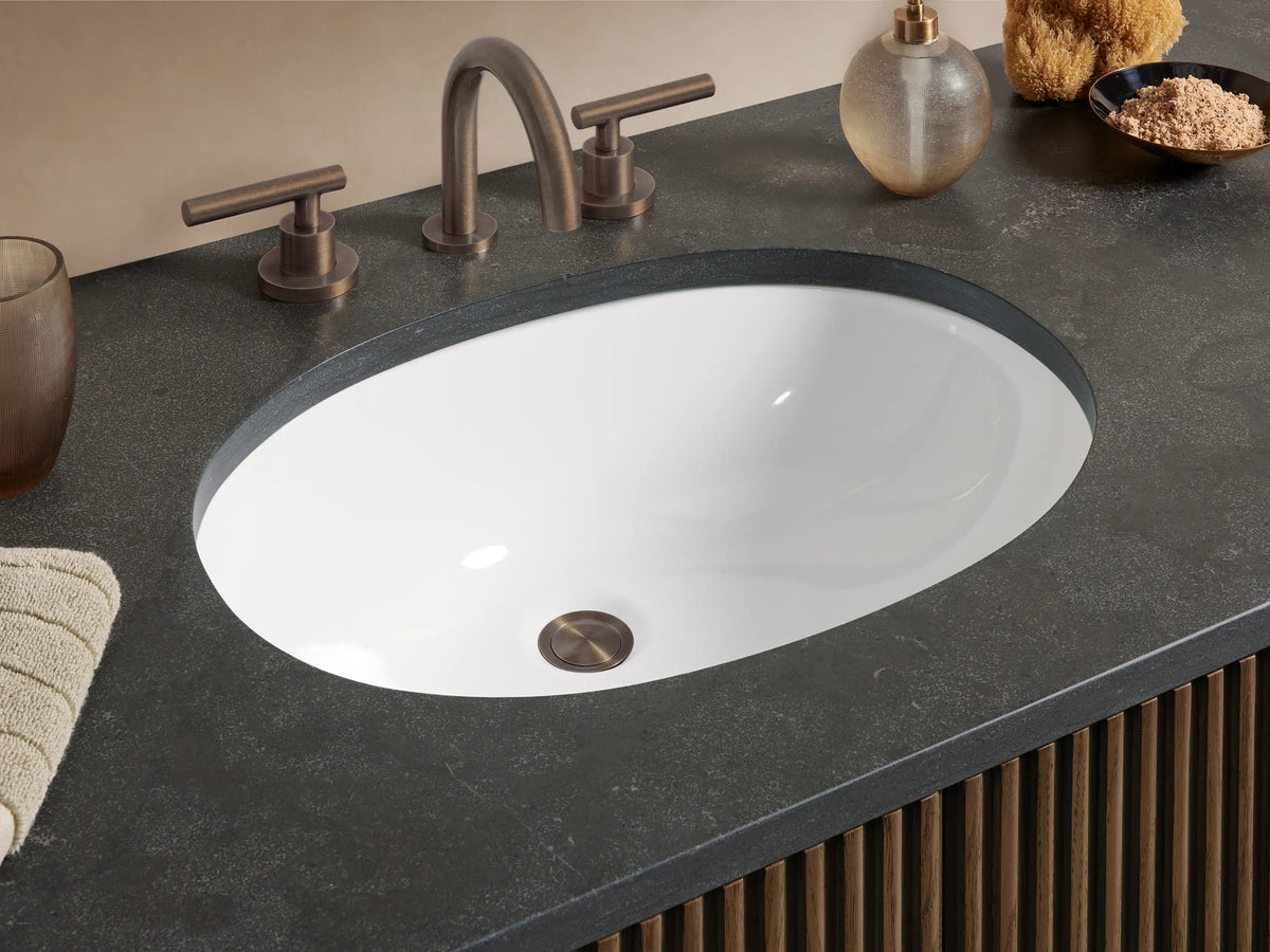 Finnley Wide Single Vanity: Dark brown fluted wood vanity with dark stone top, oval sink, six drawers, and two center doors. Bronze pulls.
