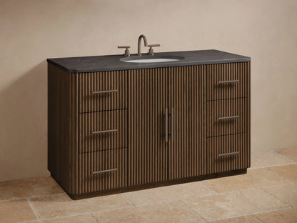 Close-up of Finnley Wide Single Vanity with dark stone top and dark brown fluted wood drawer partially open, revealing towels and bottles.