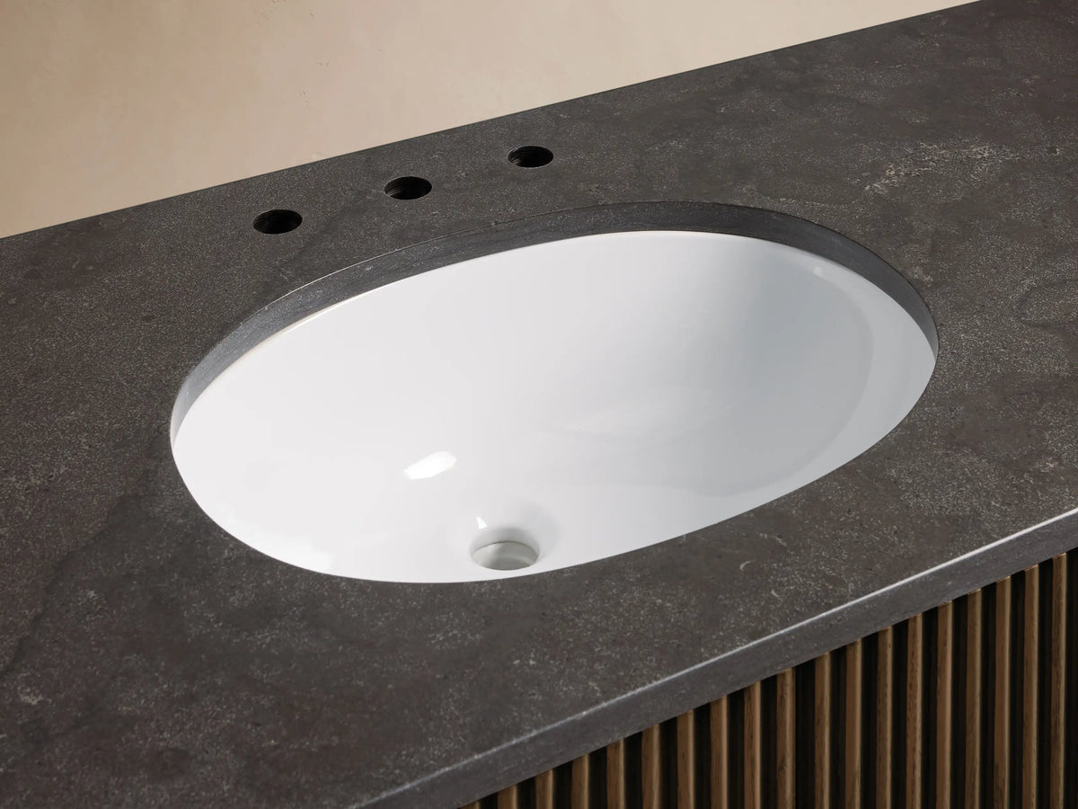 Finnley Wide Single Vanity featuring a white oval undermount sink, dark gray honed stone top, brass faucet, and ribbed wood base.