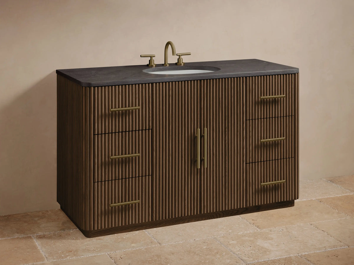 Close-up of Finnley Wide Single Vanity's dark fluted oak door, slightly open, showing white towels & a box. Brass pulls on door & drawers.
