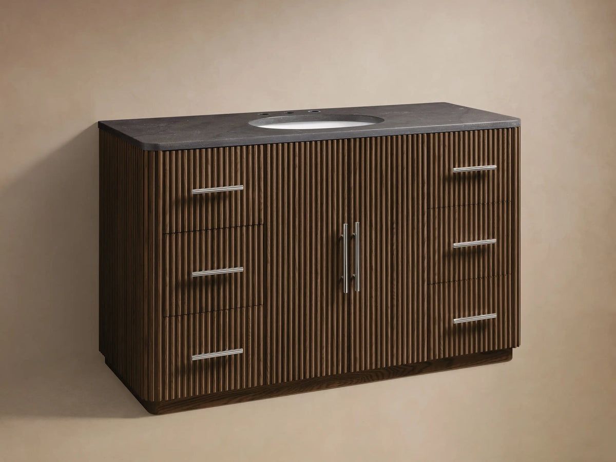 Finnley Wide Single Vanity with dark grey stone top, oval white sink, silver faucet. Dark fluted wood base, 2 doors, 6 drawers.