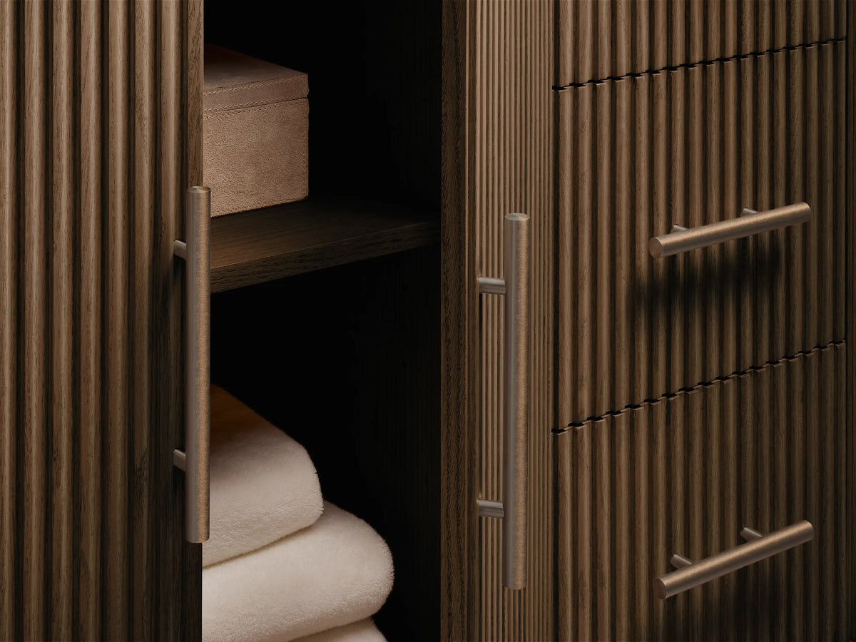 Close-up of Finnley Wide Single Vanity. White marble top, dark fluted wood base. Partially open drawer with white towels, bottles.
