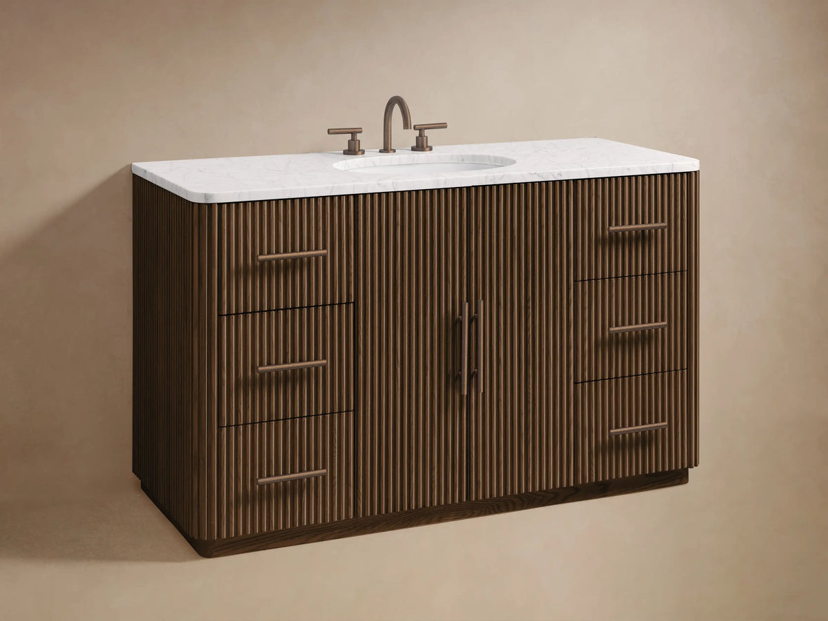 Finnley Wide Single Vanity. Close-up of ribbed dark oak wood. Left door open to shelved interior with box & white towels. Right drawers with bronze-tone pulls.