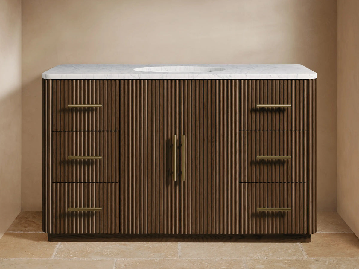 Finnley Wide Single Vanity. Dark brown ribbed wood, white marble top, brass faucet, oval sink, six drawers with brass hardware.