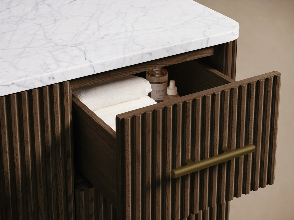 Close-up of Finnley Wide Single Vanity. Dark reeded wood door with brass handle slightly open, revealing white towels on a shelf.