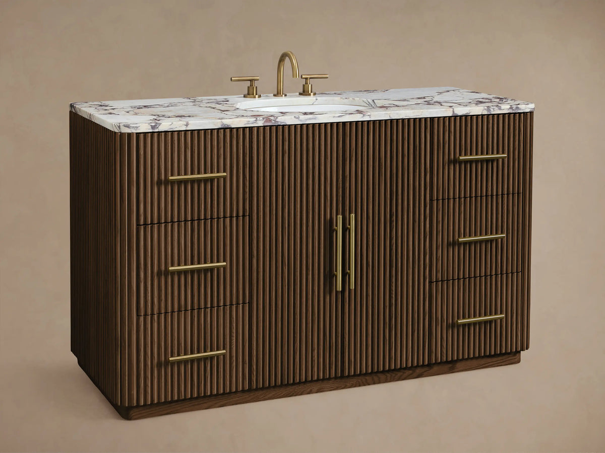 Finnley Wide Single Vanity: Dark brown fluted wood cabinet, white marble top with oval sink, brass handles, angled view.