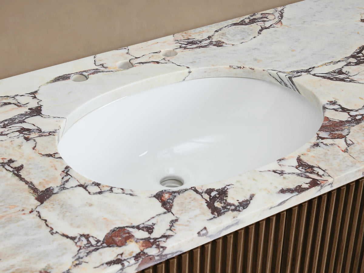 Finnley Wide Single Vanity close-up. White oval sink, white marble countertop with reddish-brown veining, brass faucet, slatted wood base.