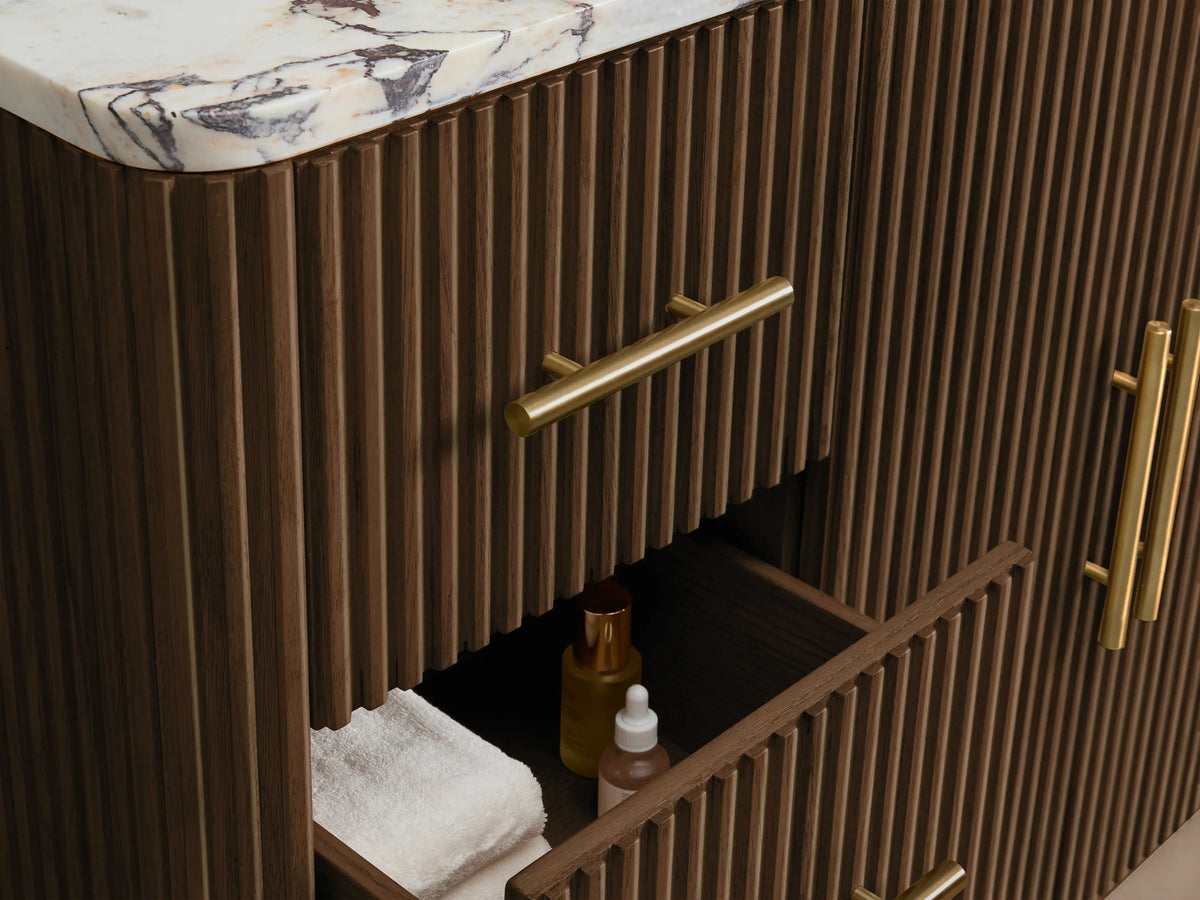 Finnley Wide Single Vanity's open fluted dark brown oak cabinet door with long brass handle, revealing interior with white towels.