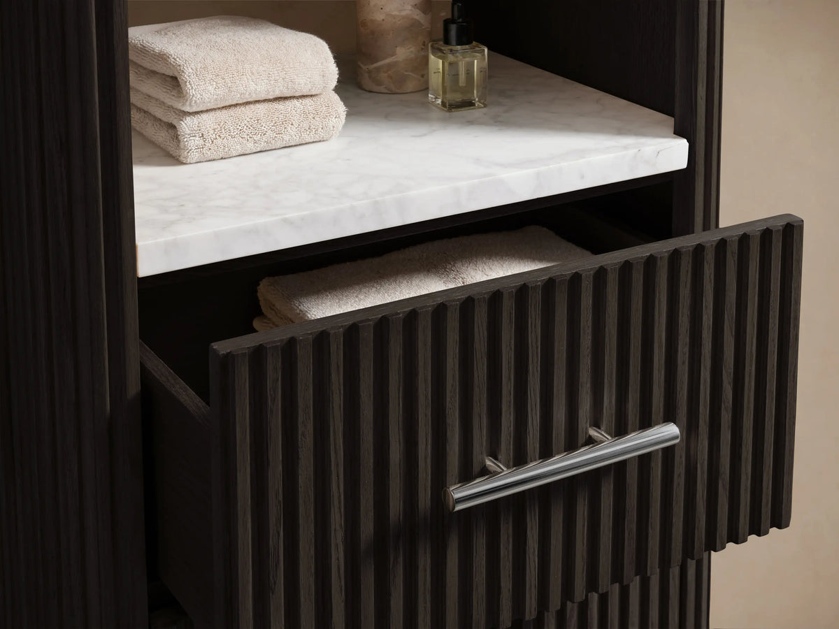 Finnley Tall Bath Cabinet: Dark brown wood cabinet with three white open shelves, three fluted drawers, silver pulls, on stone floor.
