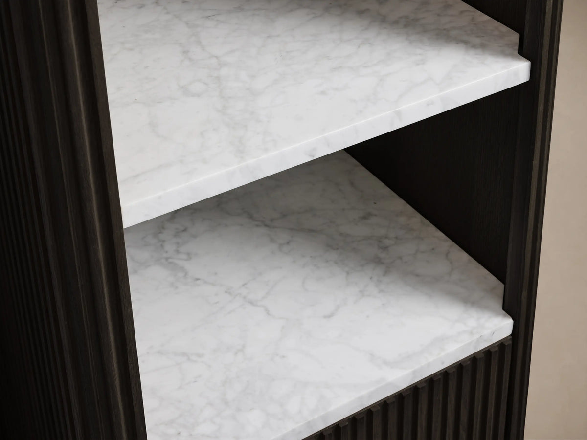 Finnley Tall Bath Cabinet, close-up. Dark fluted wood drawer open with towels. White Carrara marble shelf above with towels, soap.