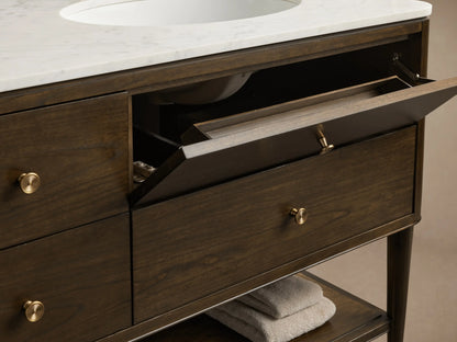 Close-up, high-angle of dark brown Laurent Double Vanity. White marble top, brass knobs. Open drawers reveal towels, perfume, comb.