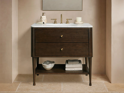Laurent Single Vanity: Dark brown wood, white marble top, oval sink, brass hardware, open shelf with towels, bathroom setting.