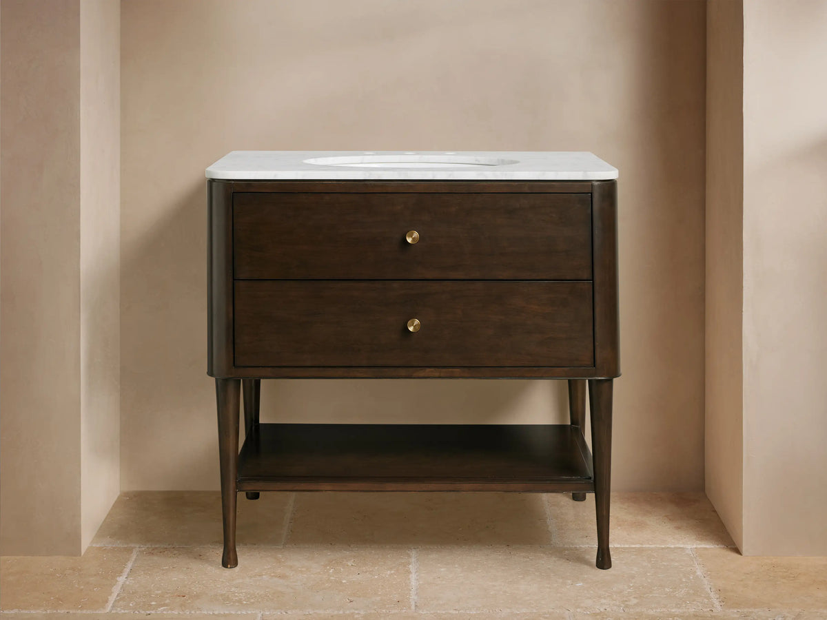 Laurent Single Vanity: Dark brown wood, white marble top, oval sink, brass hardware, open shelf with towels, bathroom setting.