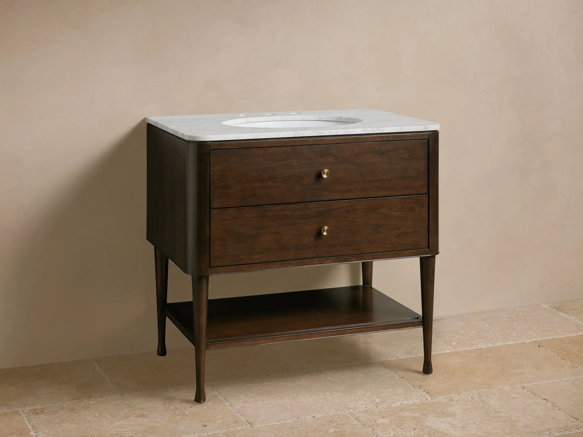 Laurent Single Vanity: dark wood frame, white marble top with oval sink & gold faucet, two drawers, lower open shelf.