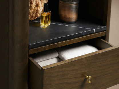 Tall Laurent bath cabinet, dark Bahasa Brown wood, black stone top. Features 3 open shelves with decor & 3 drawers with brass pulls.