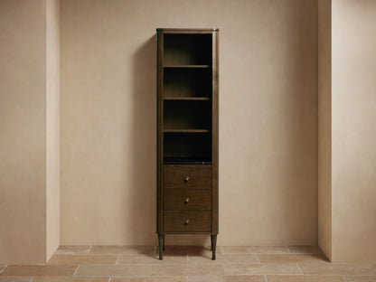 Laurent Tall Bath Cabinet: dark Bahasa Brown wood, with four open shelves holding decor and three drawers below, against a light wall.