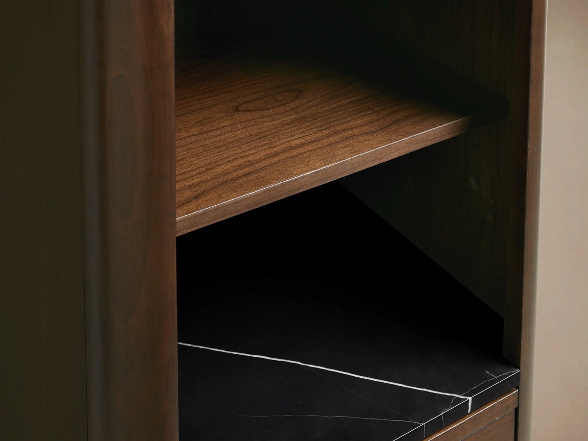 Laurent Tall Bath Cabinet in Bahasa Brown cherry wood. Black Marquina marble shelf with white veining, perfume, sponge. Open drawer reveals white towels, bronze knob.