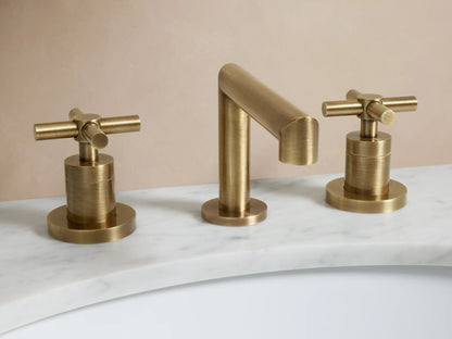 Lomas Faucet in antique brass finish with a central spout and two cross-styled handles on a marble countertop.
