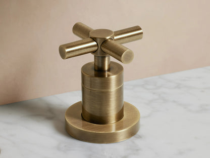 Lomas Faucet in antique brass finish with a central spout and two cross-styled handles on a marble countertop.