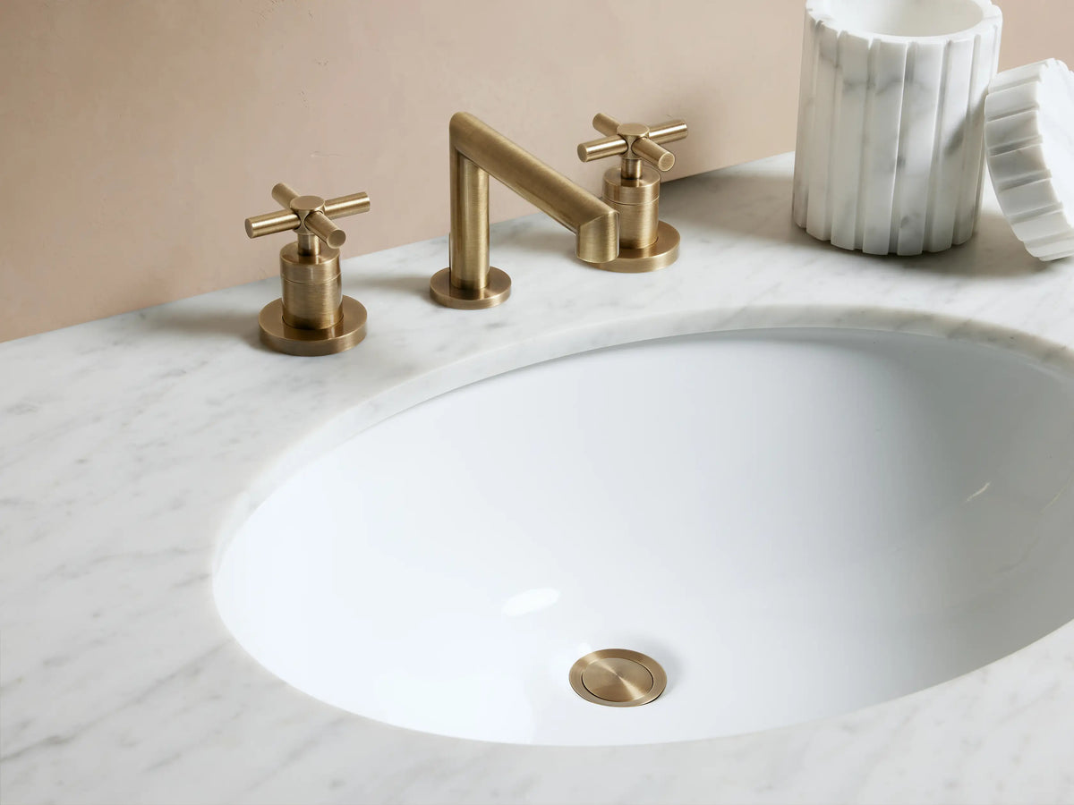 Circular pop-up drain from Lomas Faucet made of antique brass with a polished surface, set against a white background.