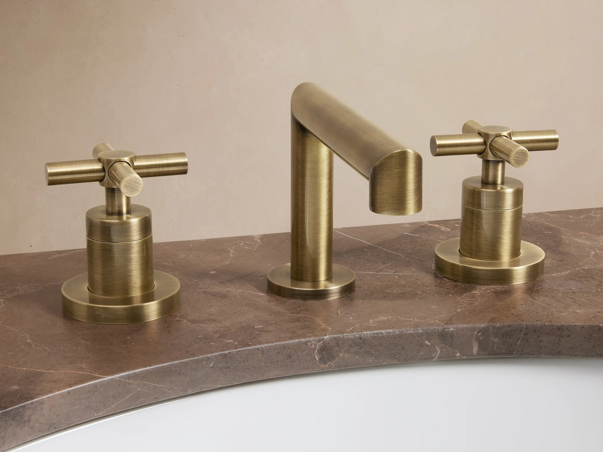 Lomas Faucet in antique brass finish, featuring a cylindrical spout and two cross-styled handles on a dark countertop.