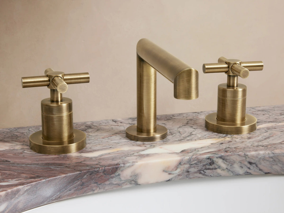 Brass-finished Lomas Faucet set on marble countertop; includes central spout and two cross-styled handles in antique brass.