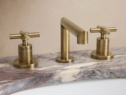 Brass-finished Lomas Faucet set on marble countertop; includes central spout and two cross-styled handles in antique brass.