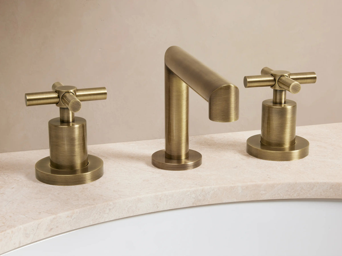 Lomas Faucet in antique brass finish with central spout and two cross-shaped handles on marble surface.