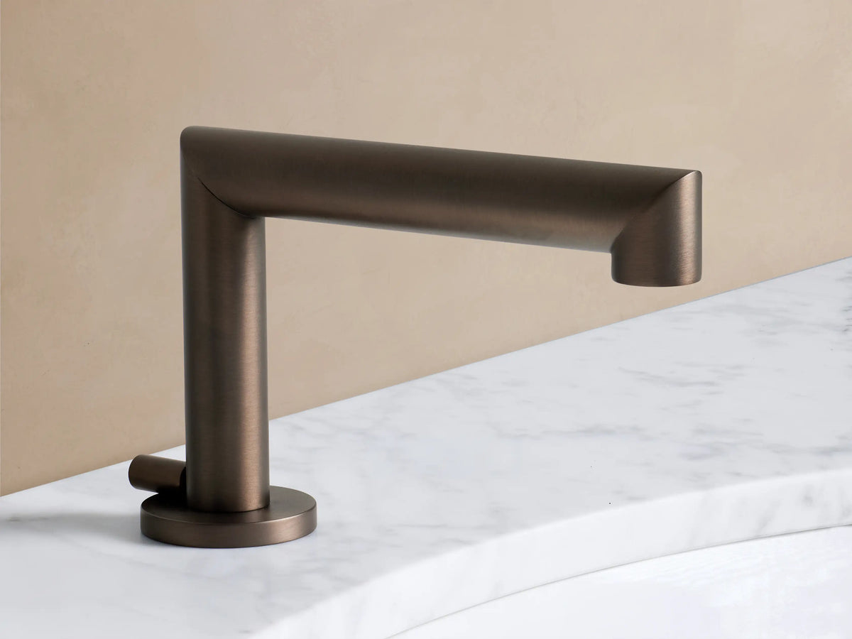 Angled close-up of a Lomas Faucet handle in Antique Bronze, featuring a distinct cross-style, on a white marble counter.