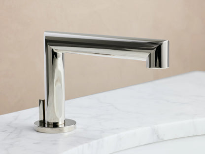 Polished nickel Lomas Faucet handle with a cross design on a white marble surface, reflecting light, against a beige background.
